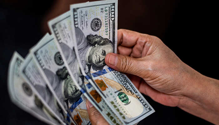 21 اکتوبر 2022 کو ایک شخص منیلا، فلپائن میں کرنسی ایکسچینج اسٹور پر امریکی ڈالر دکھا رہا ہے۔ - رائٹرز