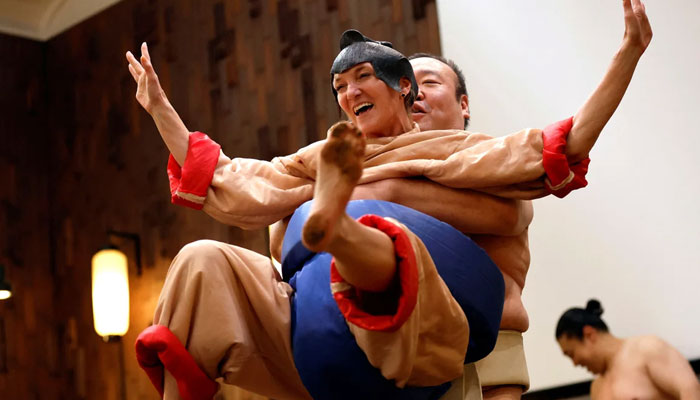 Nadine - a 43-year-old tourist from the US, wearing a sumo wrestler costume - tries to spar against former sumo wrestler Towanoyama on the sumo ring in front of tourists from abroad at Yokozuna Tonkatsu Dosukoi Tanaka in Tokyo, Japan.—Reuters