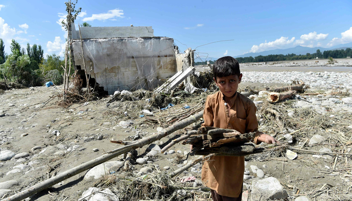 A boy carries wood near a damaged house along a river following heavy monsoon rains in Mingora, a town in Pakistan´s northern Swat valley on August 28, 2022. — AFP