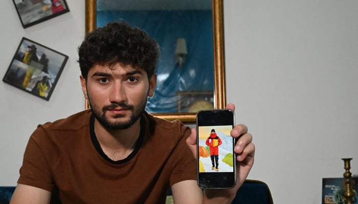 This photo taken on June 27, 2023 shows mountaineer Shehroz Kashif displaying his picture on a phone during one of his expeditions after an interview with AFP inside his home in Lahore.