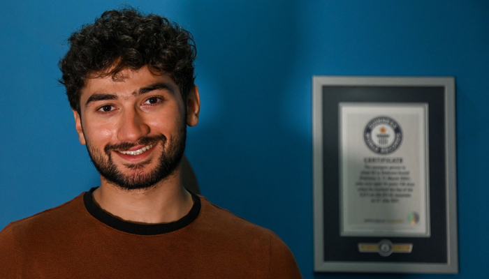 This photo taken on June 27, 2023 shows mountaineer Shehroz Kashif posing for a picture next to his Guinness record certificates during an interview with AFP inside his home in Lahore.