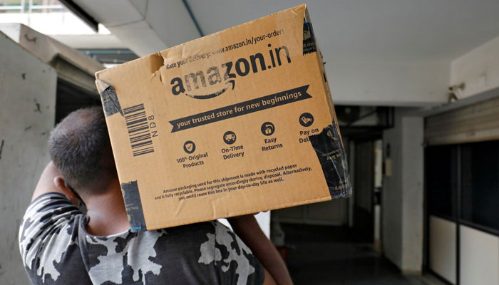 A delivery worker carries an Amazon package to deliver it to a customer at a residential apartment in Ahmedabad, India, March 17, 2021. — Reuters
