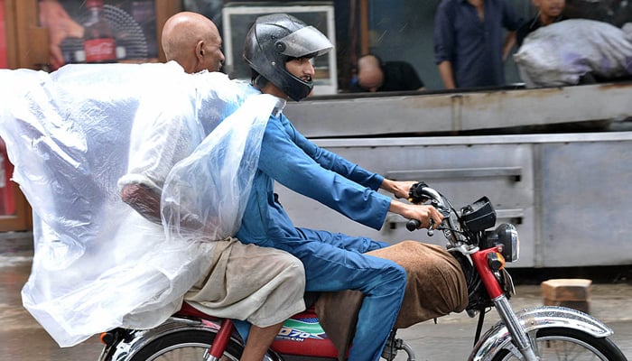 Motorcyclists covers by polythene sheets to protect themselves during rain in Lahore on July 6, 2023. — APP