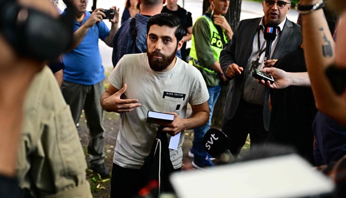 This picture shows Ahmad A. (C) outside the Isaeli embassy in Stockholm, Sweden, surrounded by journalists on July 15, 2023, after he chose not to burn the books but to hold a manifestation holding a Quran in his hand. — AFP
