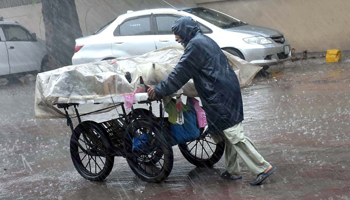 An aged person pushing his handcart loading with vegetable during heavy rain in Sialkot. —APP/file