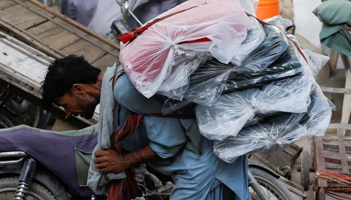 A labourer bends over as he carries packs of textile fabric on his back to deliver to a nearby shop in a market in Karachi, Pakistan June 24, 2022. — Reuters