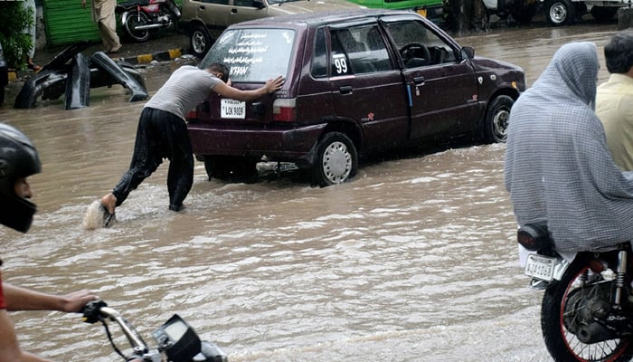 Man pushes a car breaks down due to submerged rainwater in Lahore on July 22, Saturday. — NNI