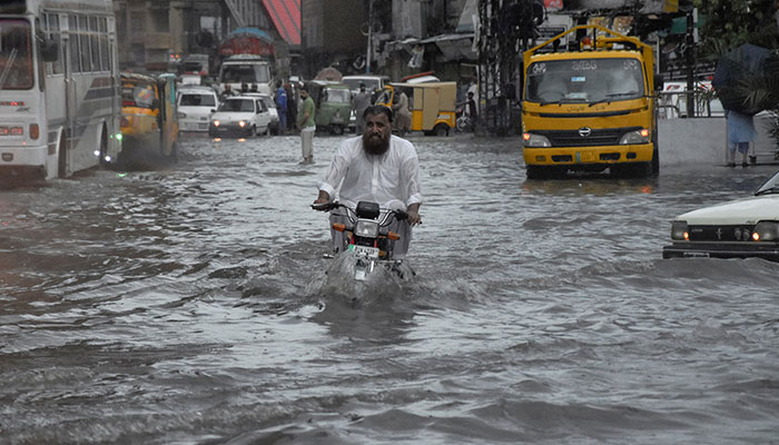 راولپنڈی، پاکستان میں 19 جولائی، 2023 کو مون سون کے موسم کے دوران سڑک کے ساتھ سیلابی پانی کے درمیان ایک شخص موٹر سائیکل پر سوار ہو رہا ہے۔ — رائٹرز