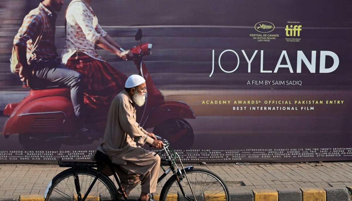 A man rides a bicycle with the Pakistani movie Joylands poster in the background. — AFP