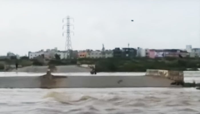 Two men seen standing on a structure at Korangi Causeway while water flows under it. — YouTube/Geo News screengrab