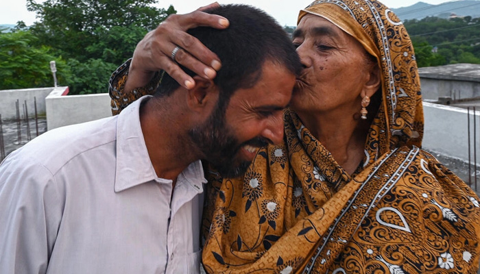 Muhammad Naeem Butt, who gave up on a perilous attempt to reach Europe, is kissed by his mother Razia Latif at their home in Pakistan. — AFP