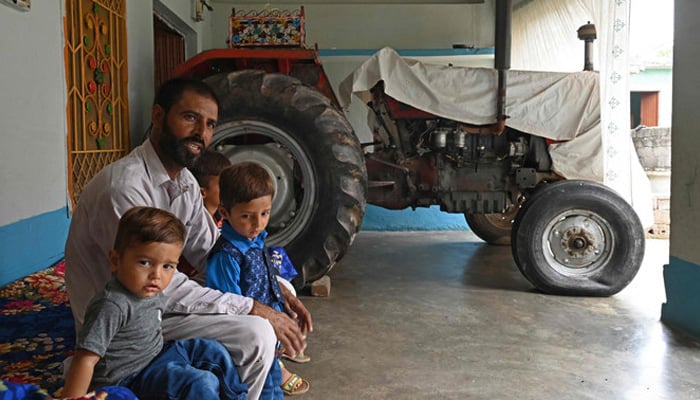 In this picture taken on July 18, 2023, Pakistani worker Muhammad Naeem Butt sits with his children at his home in Khuiratta. — AFP
