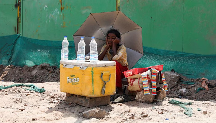 A girl selling water uses an umbrella to protect herself from the sun as she waits for customers on a hot summer day, in New Delhi, India, April 27, 2022. — Reuters