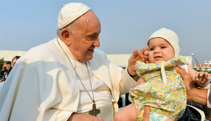 This picture released on August 5, 2023, shows Pope Francis touching a baby as he arrives before in the Sanctuary of Our Lady of Fatima, in Fatima. — AFP