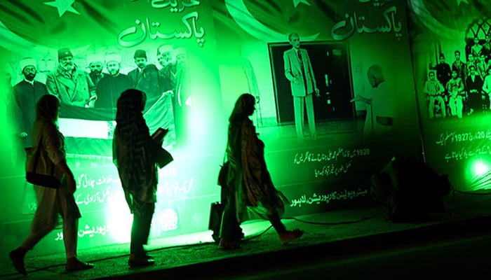 Women walk past illuminated posters illustrating Pakistans freedom fighters ahead of the countrys 76th Independence Day, in Lahore on August 12, 2023. — AFP