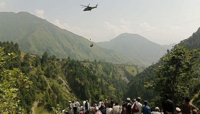 People watch as an army soldier slings down from a helicopter during a rescue mission to recover students stuck in a cable car in a village in Khyber Pakhtunkhwa on August 22, 2023. — AFP