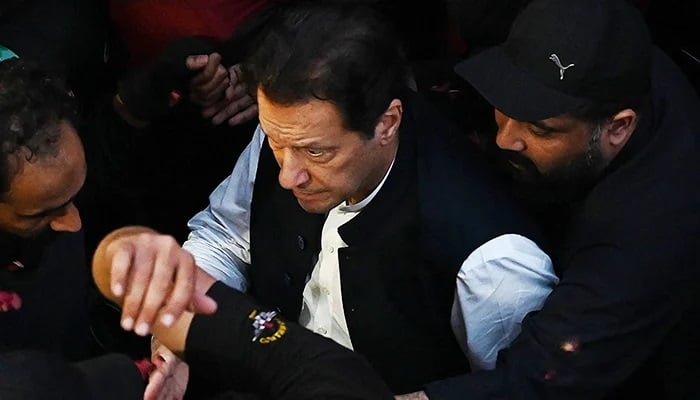 Security personnel escort former prime minister Imran Khan as he arrives to appear at the Lahore High Court on March 17, 2023. — AFP