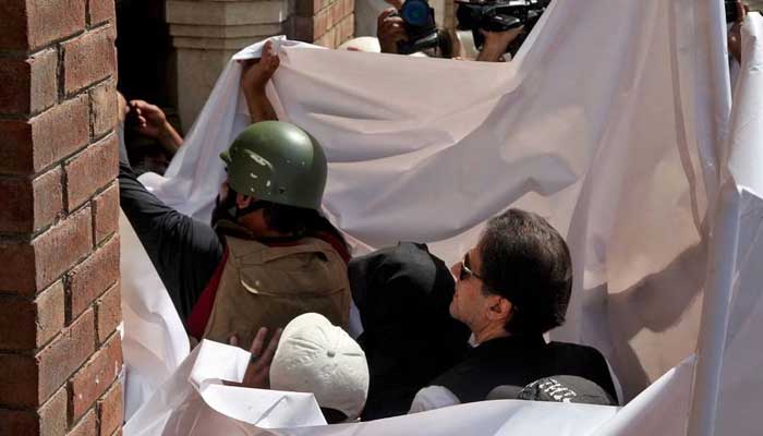 Pakistans former Prime Minister Imran Khan and his wife Bushra Bibi are covered with a white sheet as they arrive to appear at the High Court in Lahore, Pakistan, May 15, 2023. — Reuters