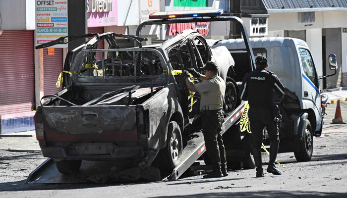 Policemen remove a burned car in front of the headquarters of the agency in charge of managing prisons (SNAI) on August 31, 2023, in Quito, Ecuador. — AFP