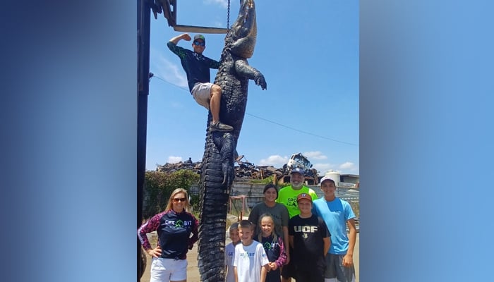 This picture, taken and released on August 26, 2023, shows a mighty alligator caught in Florida by hunters as people gather to take a photograph with the tied alligator. — Facebook/Florida Gator Hunting/Get Bit Outdoors