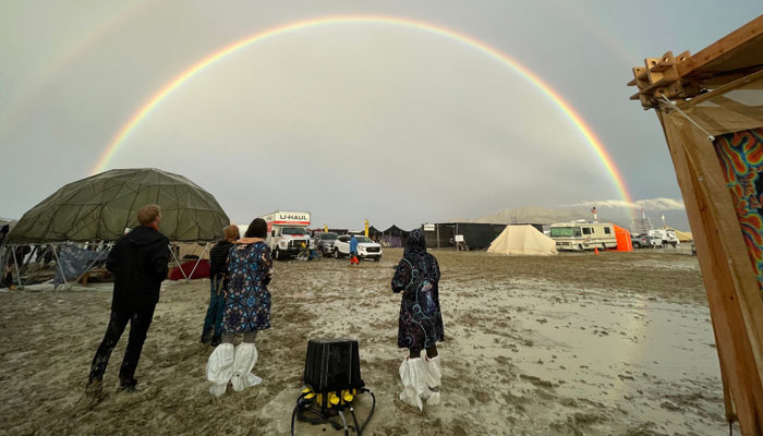 Attendees look at a double rainbow over flooding on a desert plain on September 1, 2023, after heavy rains turned the annual Burning Man festival site in Nevadas Black Rock desert into a mud pit. AFP