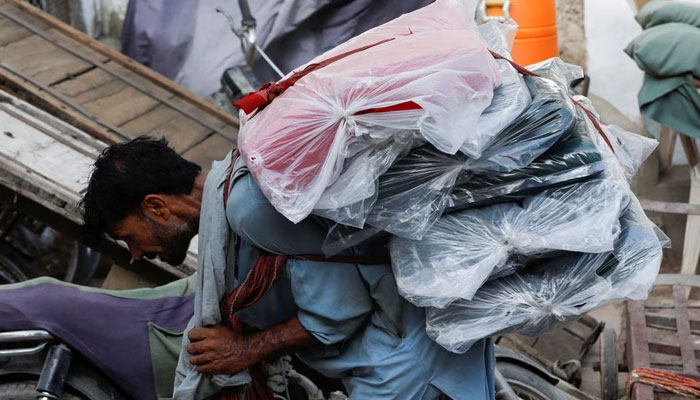 A labourer bends over as he carries packs of textile fabric on his back to deliver to a nearby shop in a market in Karachi, Pakistan June 24, 2022. — Reuters