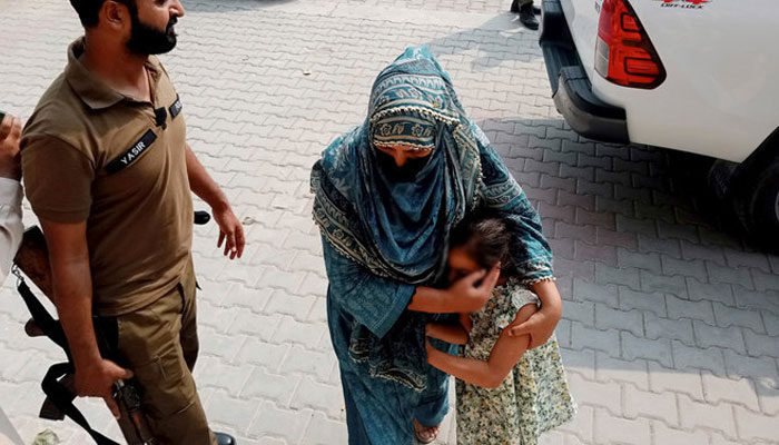 Police officers escort a relative and a child of a couple wanted by British police in connection with last months death of their 10-year-old daughter on the outskirts of London, to appear them in a court in Jhelum, about 175 kilometres (110 miles) northwest of Lahore in central Pakistan on September 12, 2023. — AFP