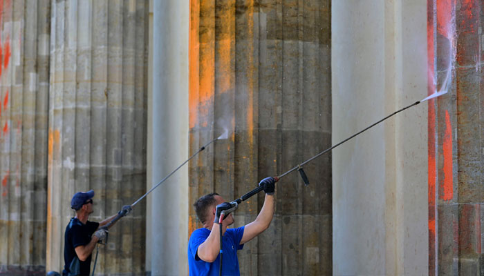 Two men remove paint from the columns of Berlin´s landmark the Brandenburg Gate on September 17, 2023 in Berlin.—AFP