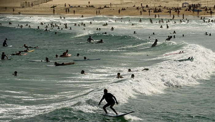 A surfer rides a wave past a crowd of people at the beach as parts of Australias east reached their hottest day in more than two years amid temperatures which rose to 40 degrees Celsius (104 degrees Fahrenheit), in Bondi Beach, Sydney, Australia, March 6, 2023. — Reuters/File