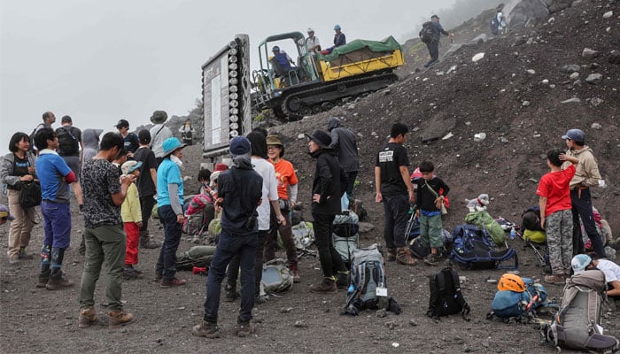 This photo taken on August 31, 2023 shows visitors taking a break from their climb on the slopes of Mount Fuji, Japans highest peak at 3,776 meters (12,388 feet), as a vehicle (C-top) used to transport various goods back and forth descends a trail. — AFP/FIle