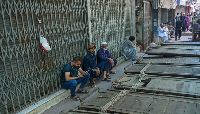Shopkeepers sit beside carts outside closed shops along a roadside in Karachi on September 2, 2023. — AFP