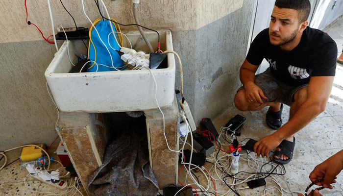 Palestinians charge their mobile phones from a point powered by solar panels provided by Adel Shaheen, an owner of electric appliances shop, as electricity remains cut during the ongoing Israeli-Palestinian conflict, in Khan Younis in the southern Gaza Strip October 14, 2023.—Reuters