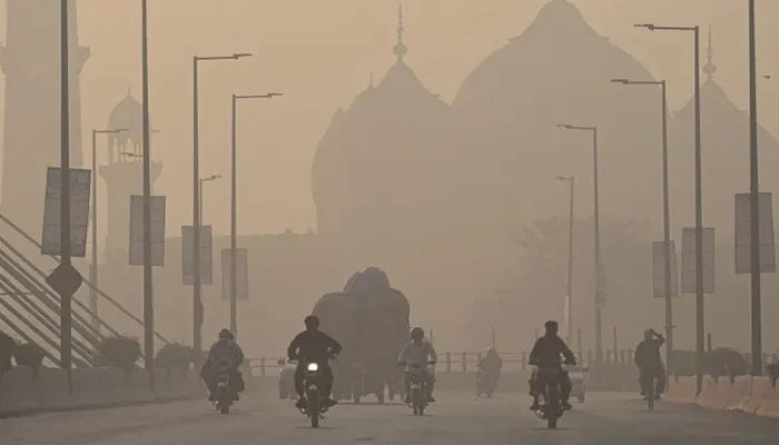 Commuters ride along a road amid smoggy conditions in Lahore on November 16, 2021. — AFP