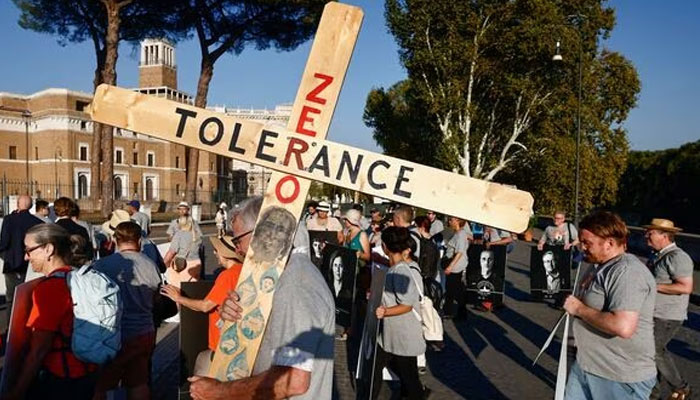 A man carries a cross as survivors of clergy sexual abuse and activities hold pictures of survivors of sexual abuse as they attend a protest near the Vatican, in Rome, Italy. —Reuters