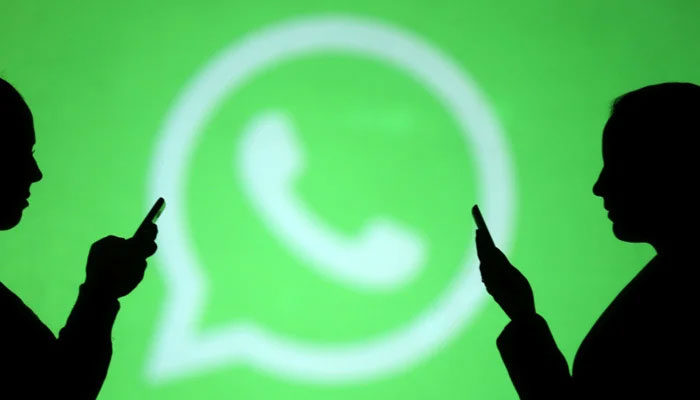 Two people use their phones with WhatsApp logo in the background. — Reuters/File