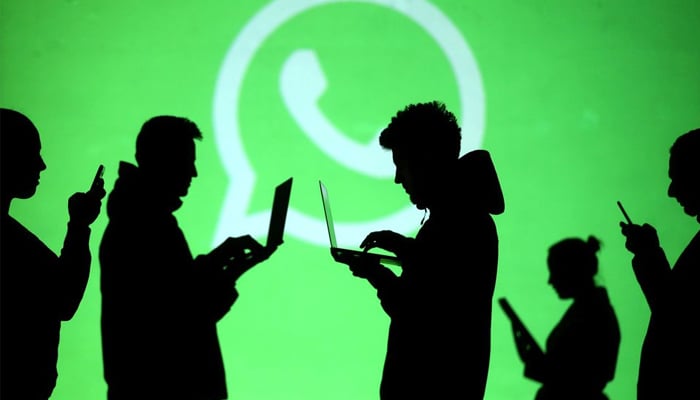Silhouettes of laptop and mobile device users are seen next to a screen projection of the Whatsapp logo in this picture illustration taken March 28, 2018. — Reuters