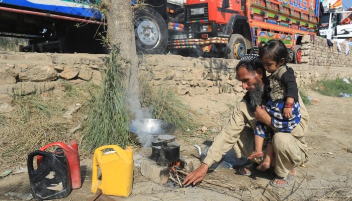 An Afghan man carries his daughter while preparing tea in front of trucks loaded with belongings outside the United Nations High Commissioner for Refugees (UNHCR) repatriation centres in Azakhel town in Nowshera, Pakistan November 3, 2023. — Reuters