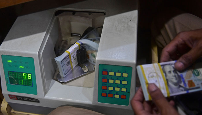 A currency exchange dealer counting $100 bills in a machine in this undated picture. — AFP/File