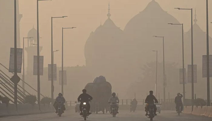 Commuters ride along a road amid smoggy conditions in Lahore on November 16, 2021. — AFP