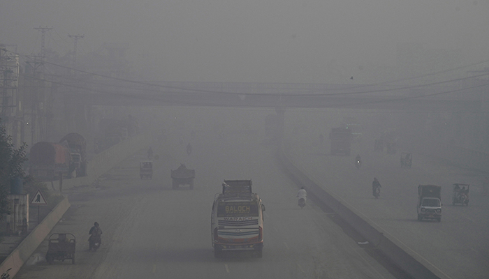 Commuters make their way along a road amid smoggy conditions in Lahore on November 14, 2023. — AFP