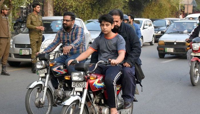 A young boy is carrying his father on motorcycle on the way at a road in Lahore. — Online/File
