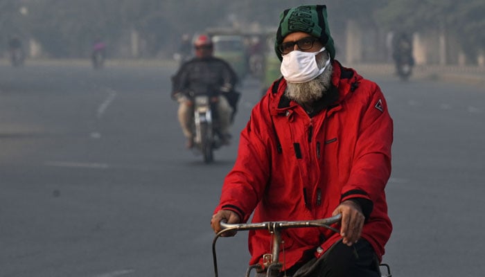 A man wearing face mask rides a bicycle, amid smoggy conditions in Lahore on November 21, 2023. — AFP