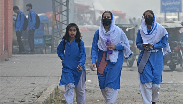 Students wearing face masks walk along a street amid smoggy conditions in Lahore on November 21, 2023. — AFP