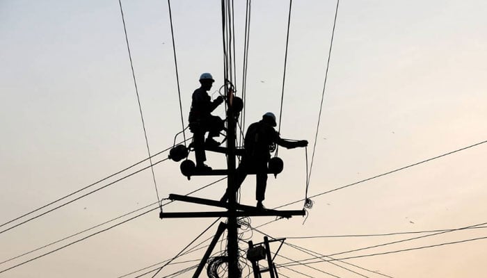 Technicians are silhouetted as they fix cables on a power transmission line in Karachi, Pakistan, January 9, 2017. — Reuters