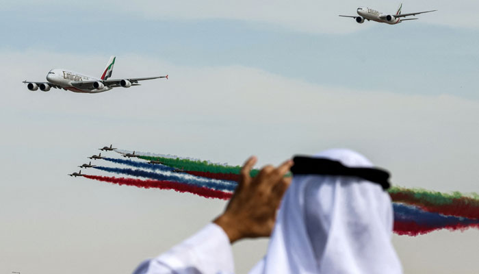 A man films with his phone as Aermacchi MB-339 trainer aircraft of the Fursan al-Emarat (UAE Knights) aerobatics team release smoke while flying over with an Emirates Airbus A380-861 (L) and another Emirates Boeing jetliner aircraft during the 2023 Dubai Airshow at Dubai World Central - Al-Maktoum International Airport in Dubai on November 13, 2023. — AFP