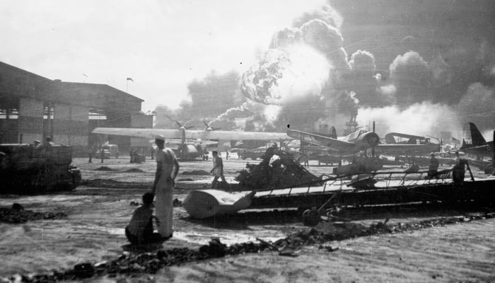 Sailors stand amid wrecked planes at the Ford Island seaplane base, watching as the destroyer USS Shaw explodes in the centre background.—Reuters