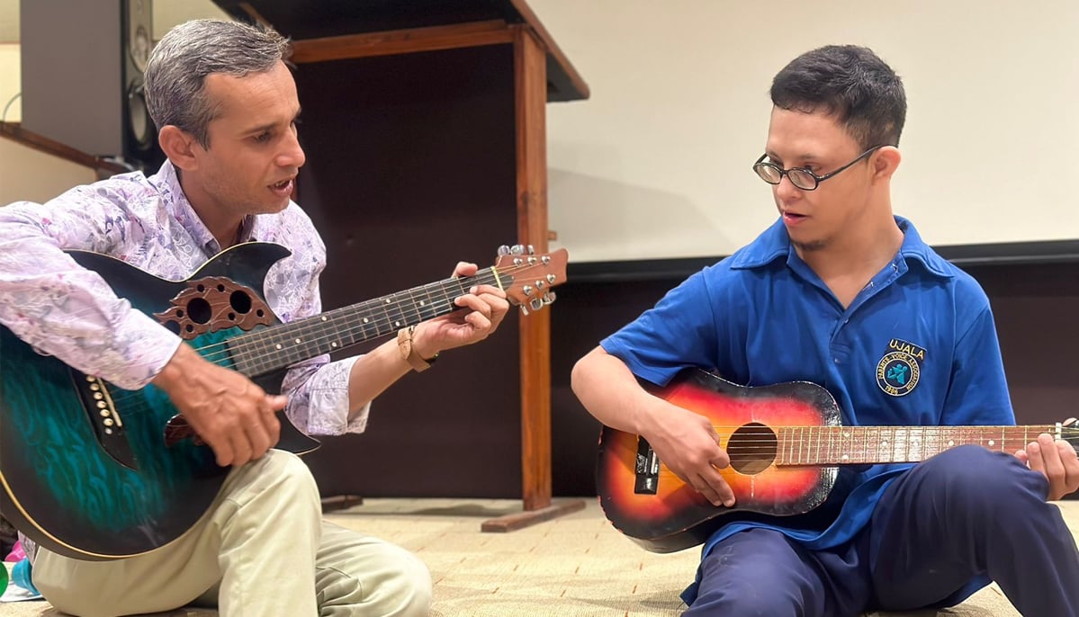 A child with Downs syndrome is seen learning how to play a guitar from his teacher in this photograph. — Facebook/Parents Voice Association - Ujala Centre