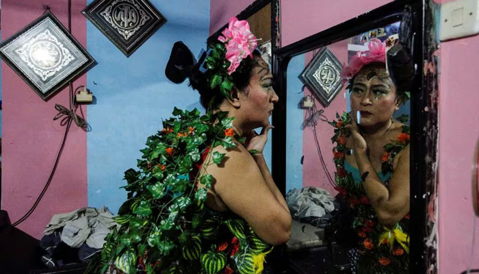 Nuke Herawati, 43, a trans woman who wears a recycled material dress to bring awareness to LGBT rights and environmental protection, looks in the mirror before a Trans Super Heroes fashion show at a traditional market in Jakarta, Indonesia, December 17, 2023. —Reuters