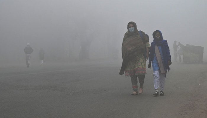 A student walks with her mother to school amid foggy weather in Lahore on December 21, 2022. — AFP