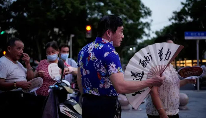 People use fans as they gather in a park amid a heatwave warning in Shanghai, China July 23, 2022. — Reuters